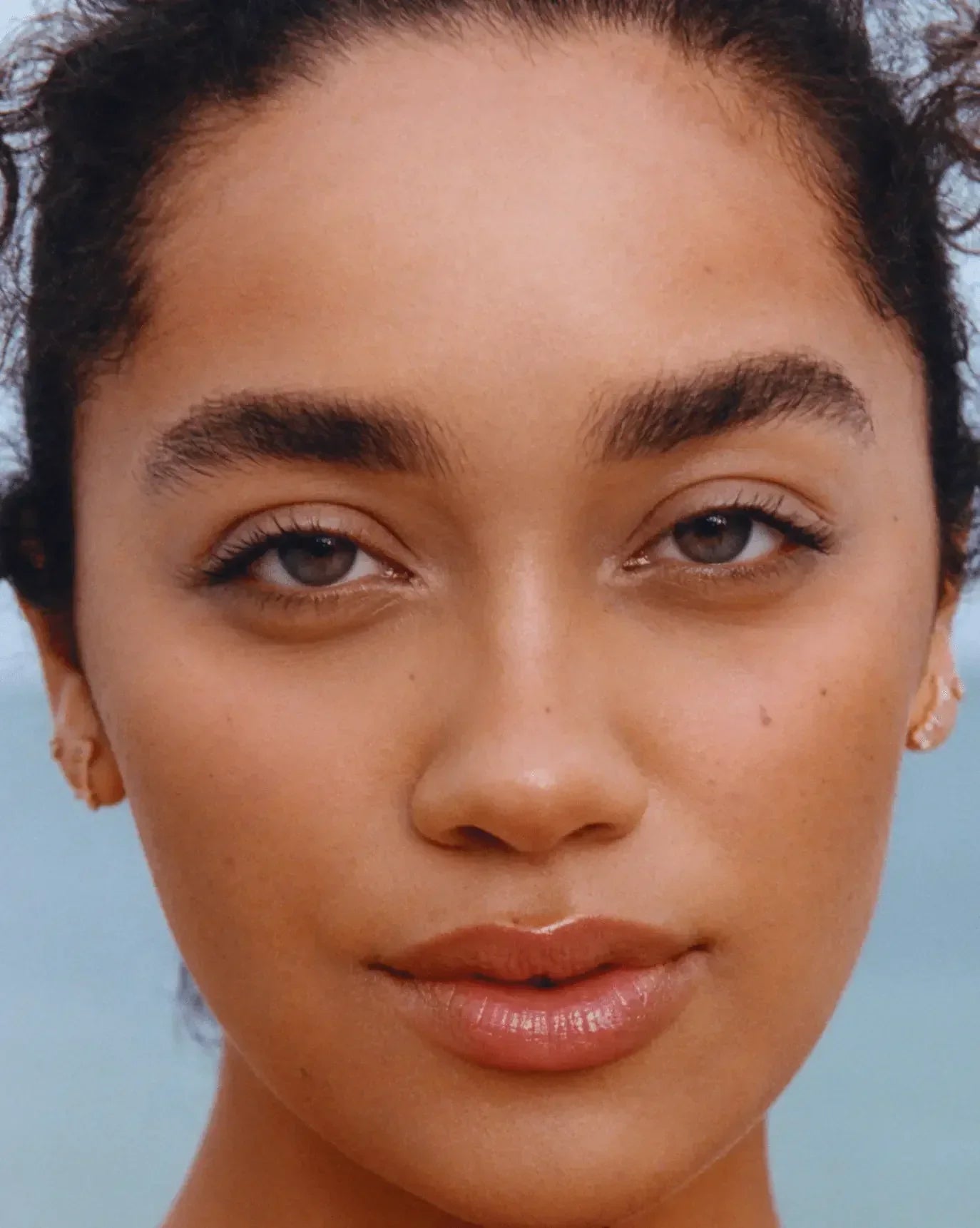 Close-up of a woman with radiant skin, natural blush, and glossy nude lips.