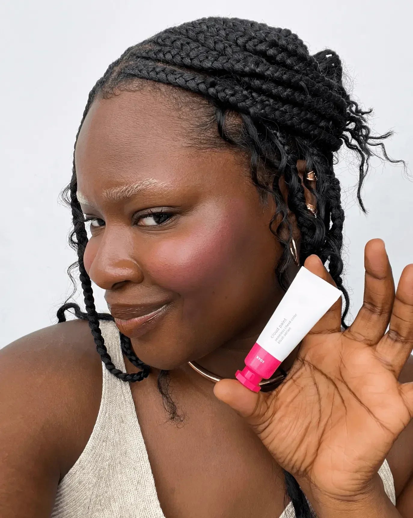 Woman with radiant, dewy finish blush in a soft pink shade, holding a tube of cream blush.