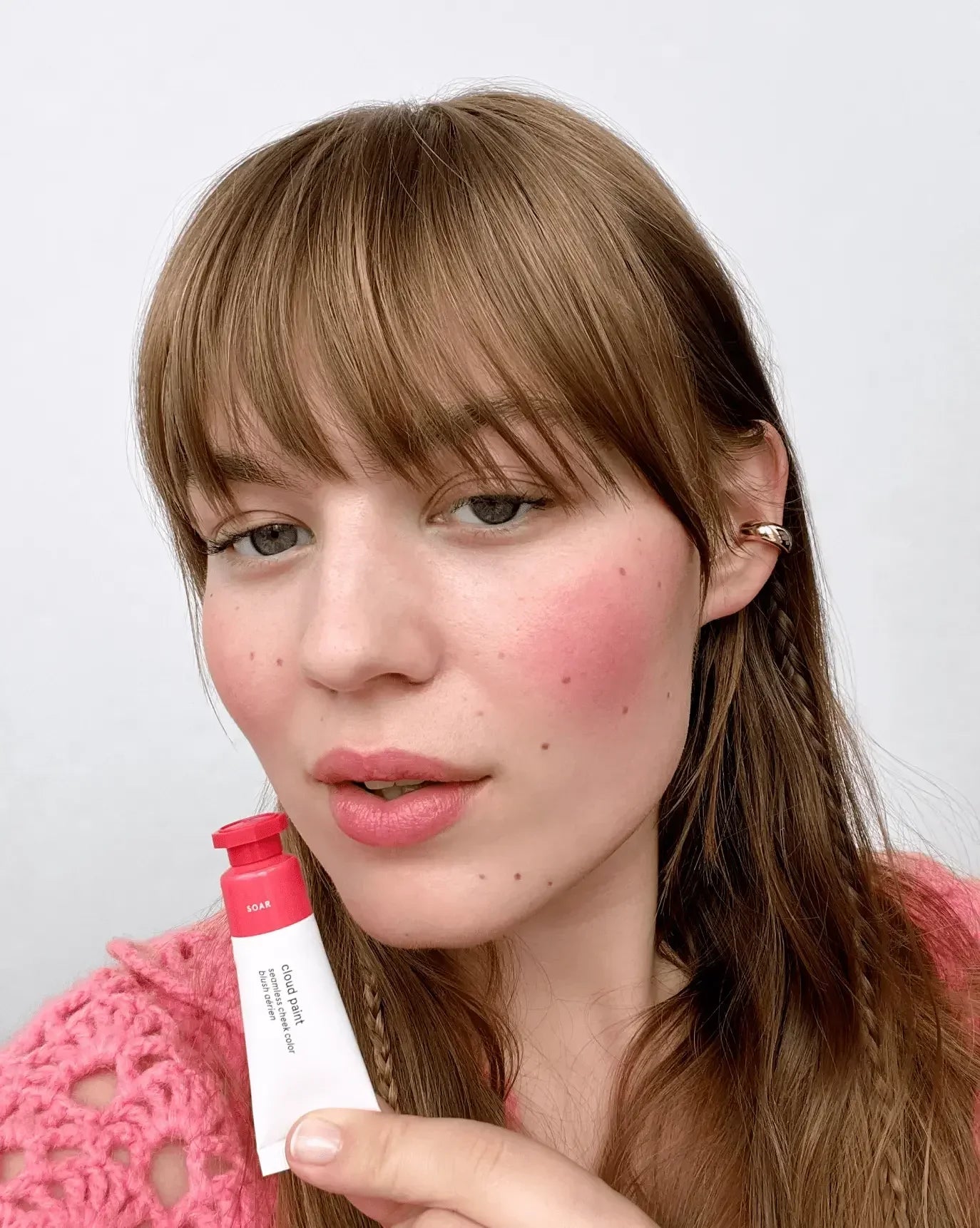 Woman with soft pink blush on cheeks holding tube of cream blush in radiant, dewy finish.