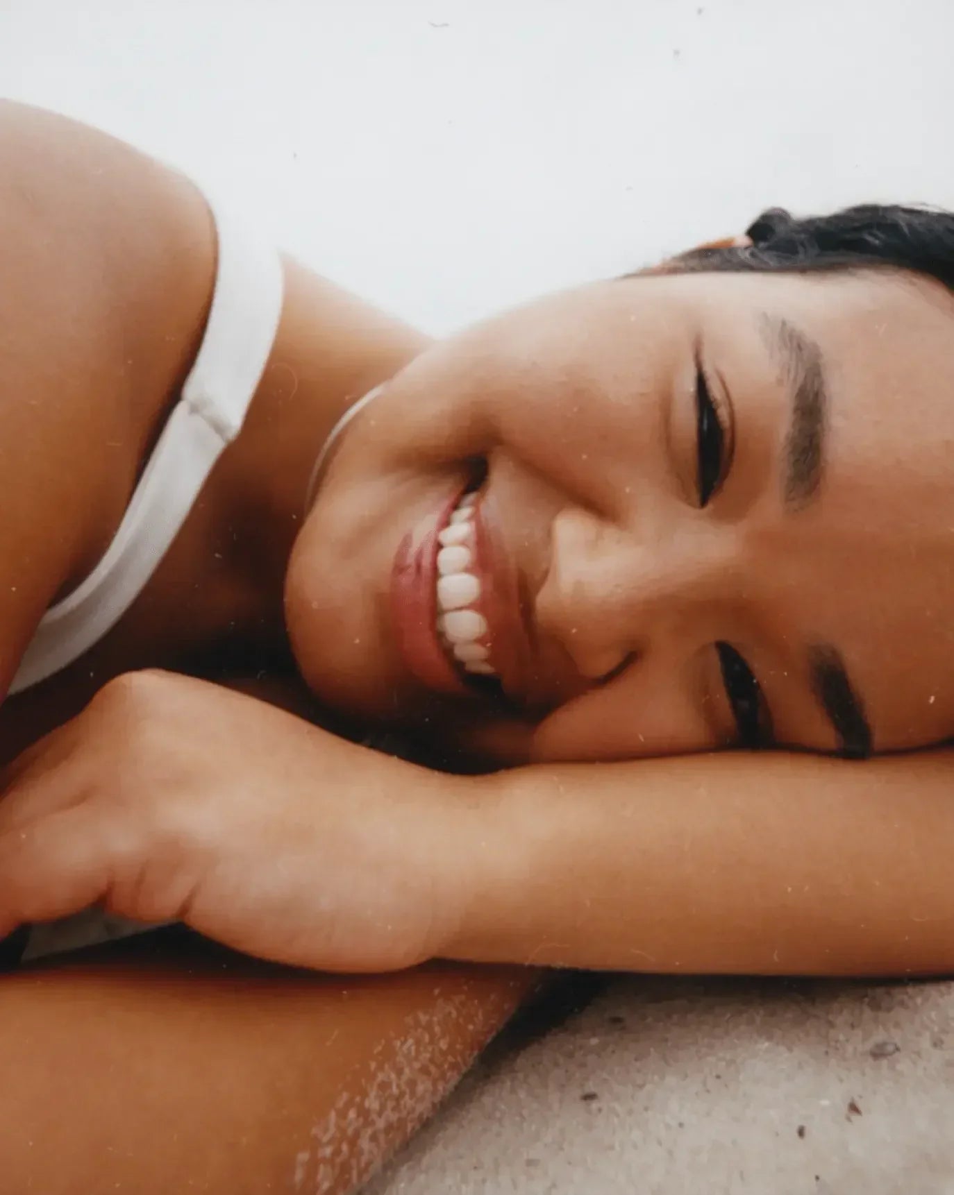 Young woman smiling with glowing, smooth skin and natural makeup, wearing a white tank top