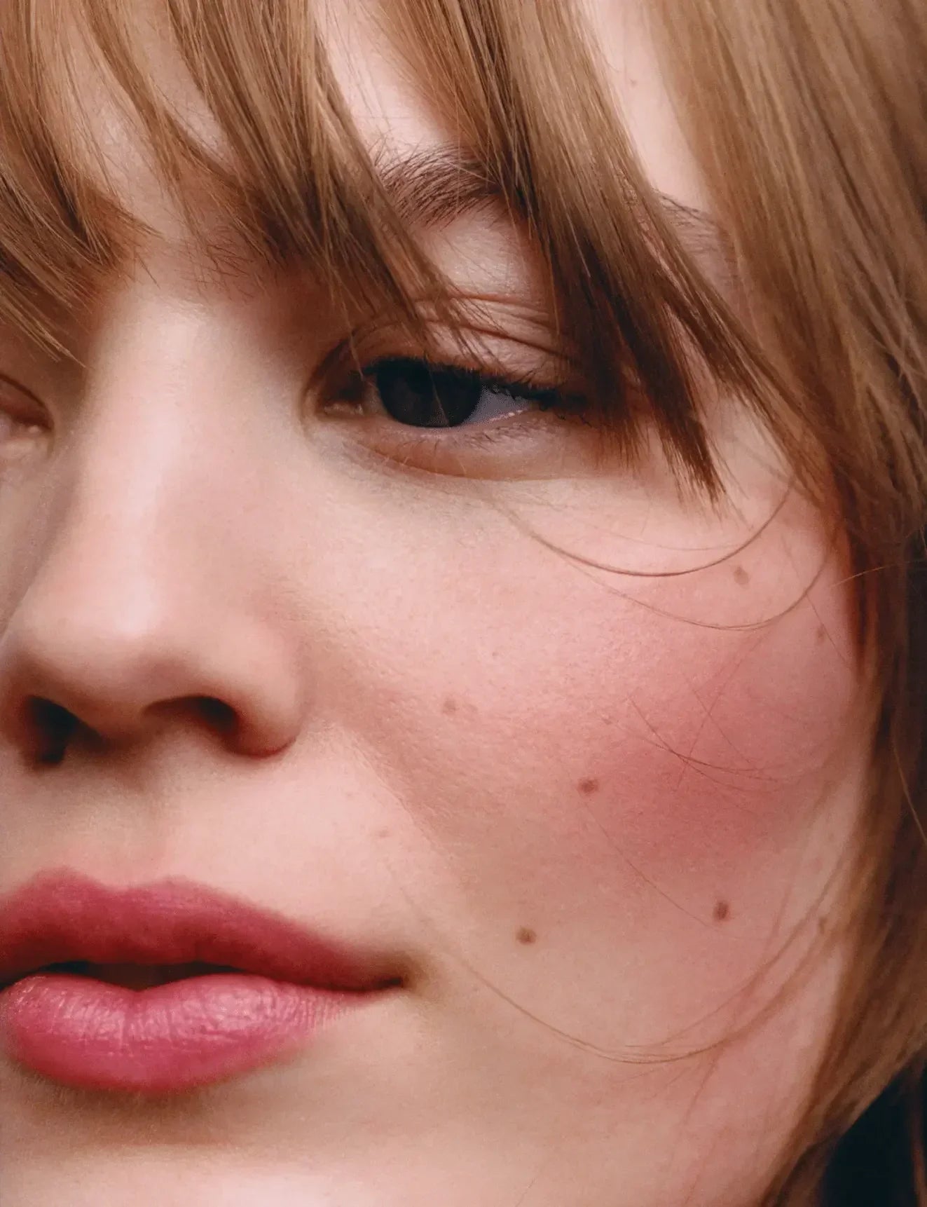 Close-up of a woman's face with soft pink blush and a natural dewy finish on her cheeks