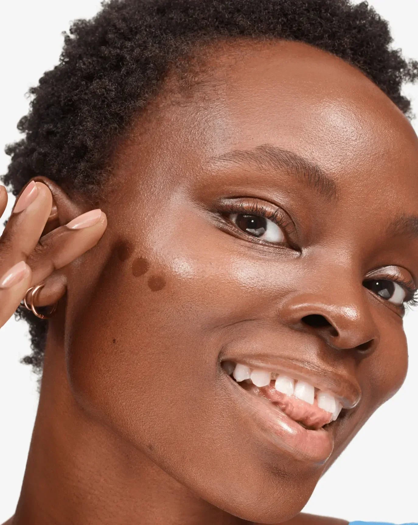 Woman applying creamy, dewy blush dots to cheek on radiant, smooth skin