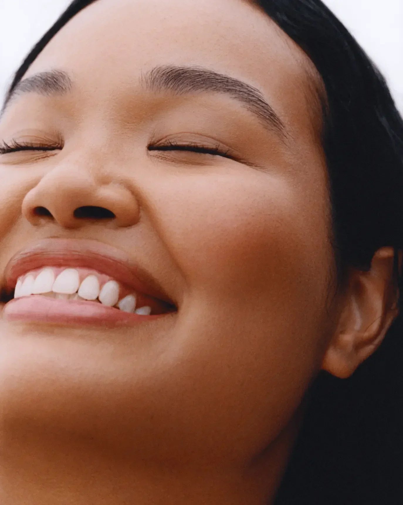 Smiling woman with dewy, peach-toned blush and flawless, radiant skin