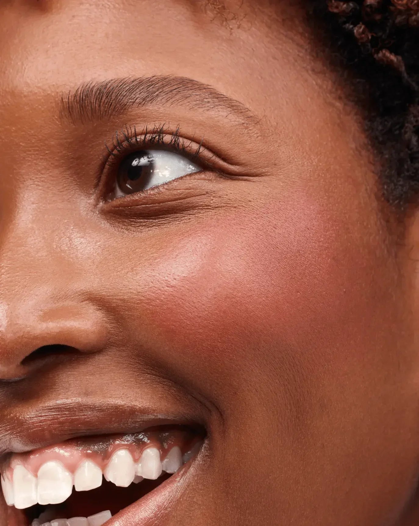 Close-up of glowing skin with rosy, creamy blush and soft, dewy makeup finish on cheek.