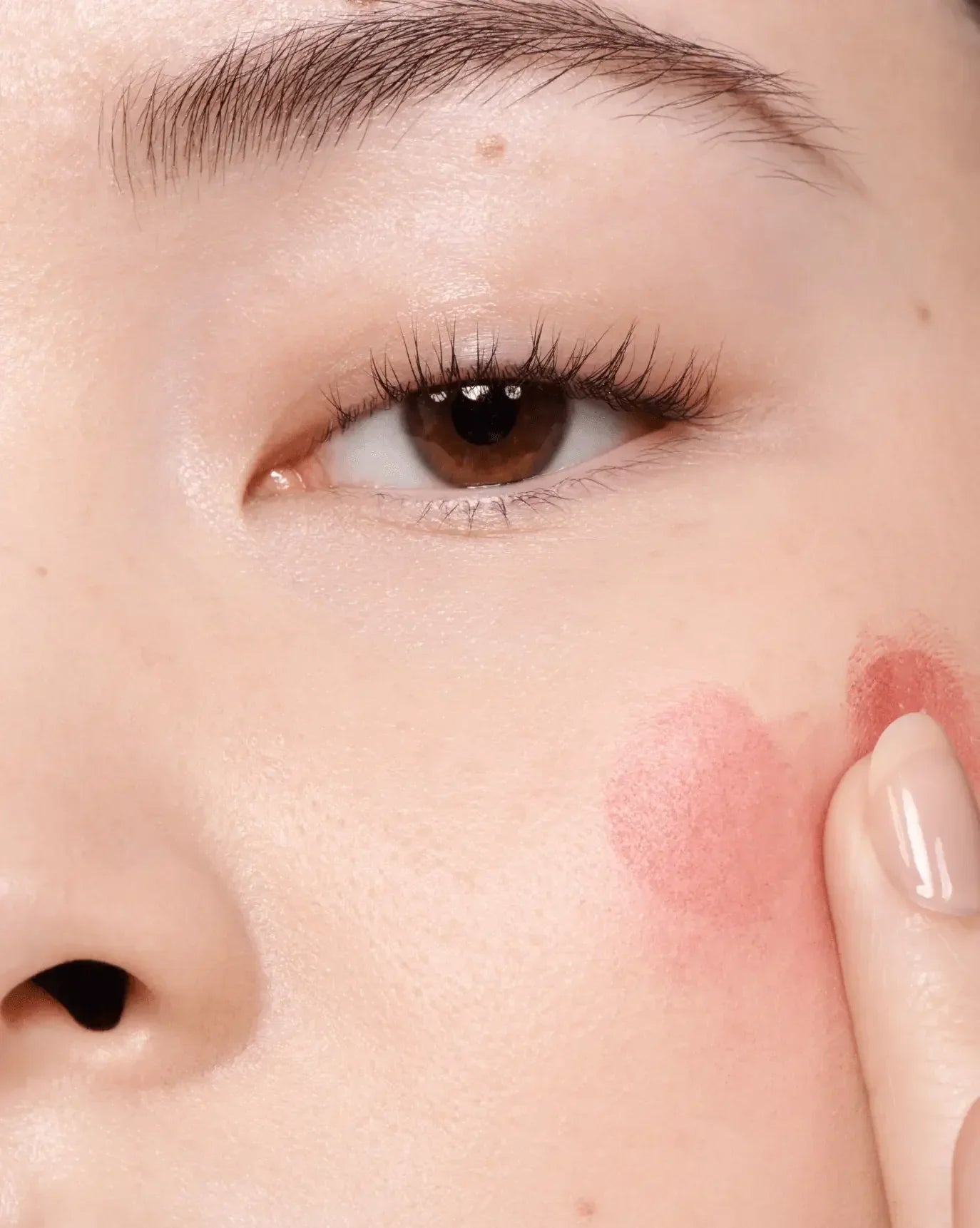Applying creamy rosy blush with dewy finish to cheek on smooth, radiant skin