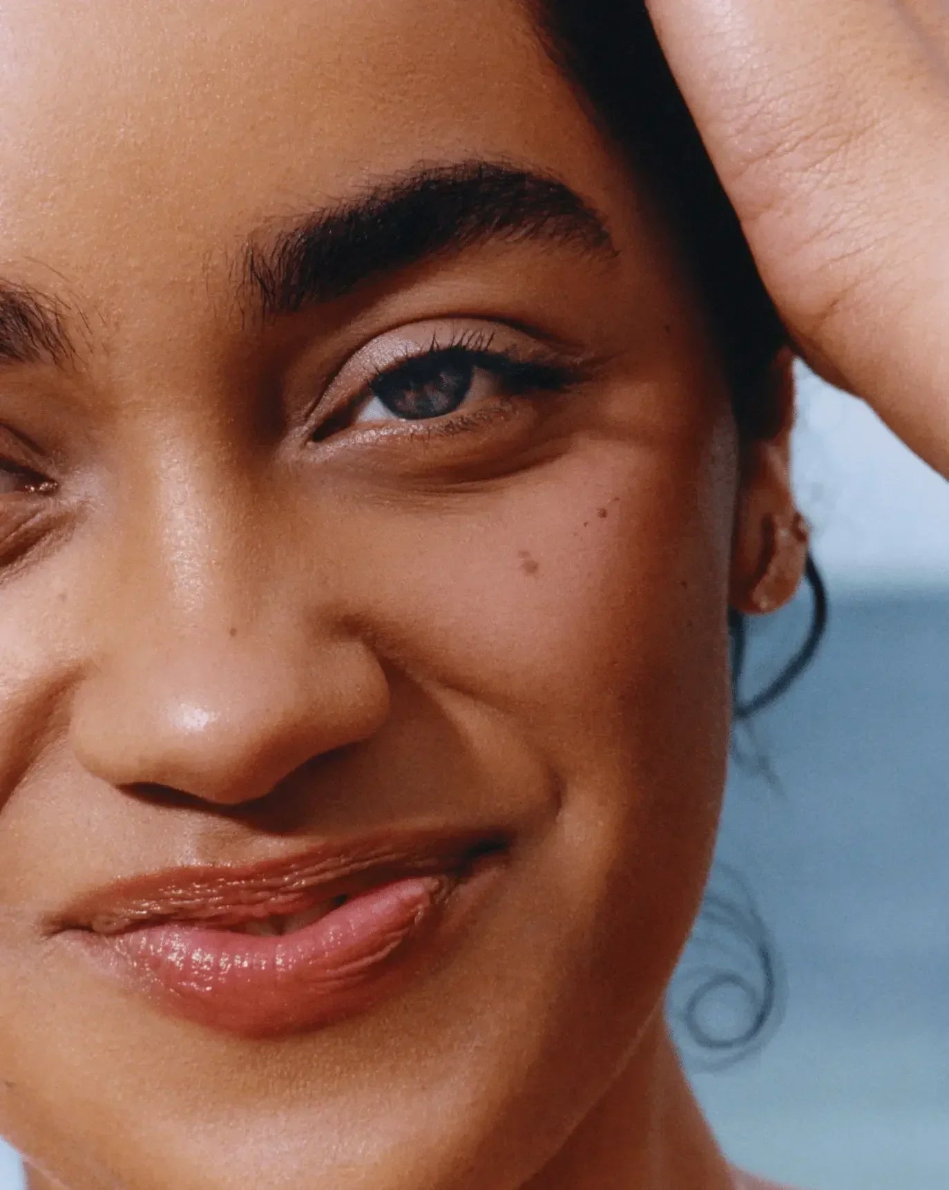 Close-up of woman with radiant skin, natural blush, and glossy lips highlighting dewy makeup finish.