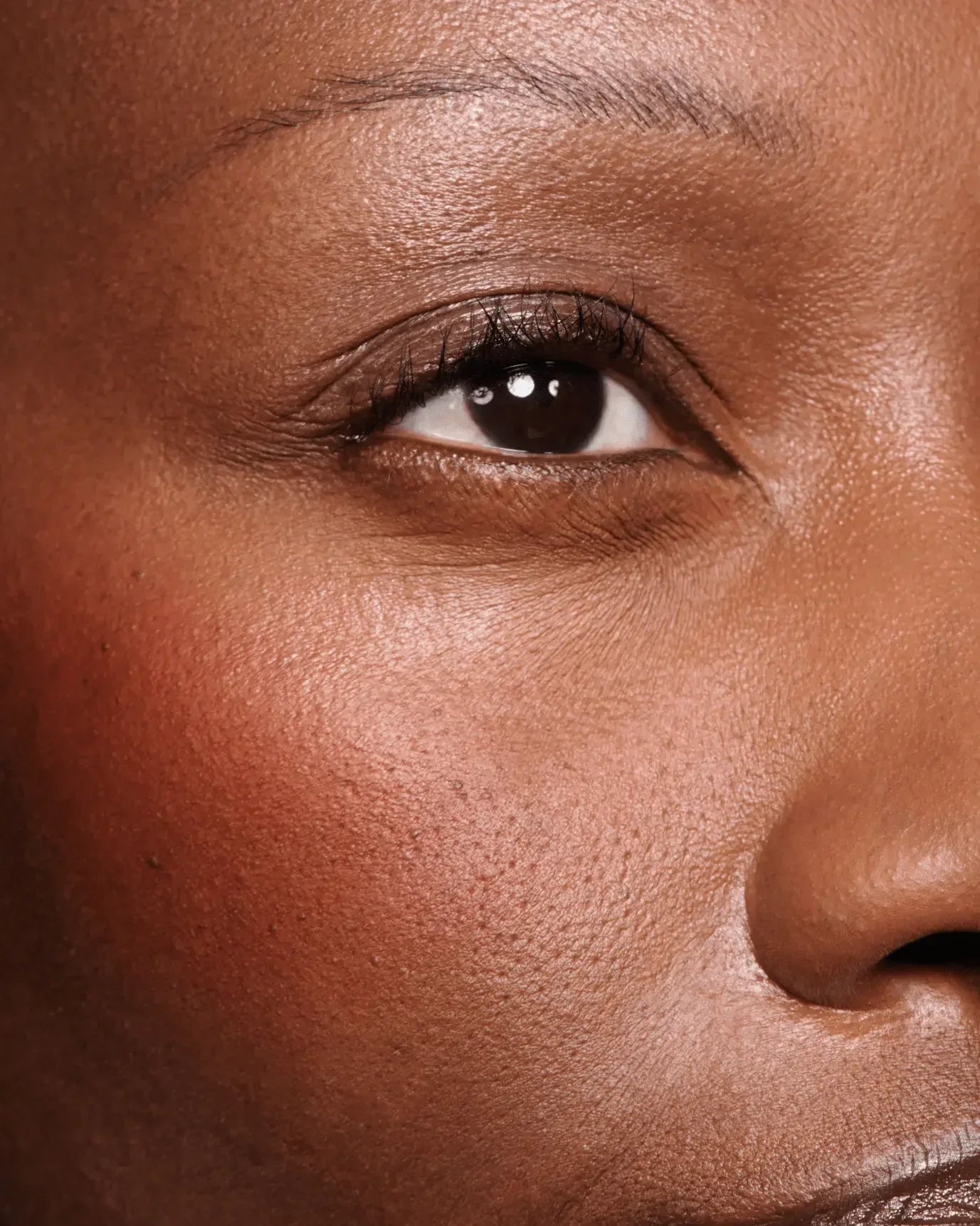Rich coral cream blush with a dewy finish on deep skin, soft radiant texture close-up