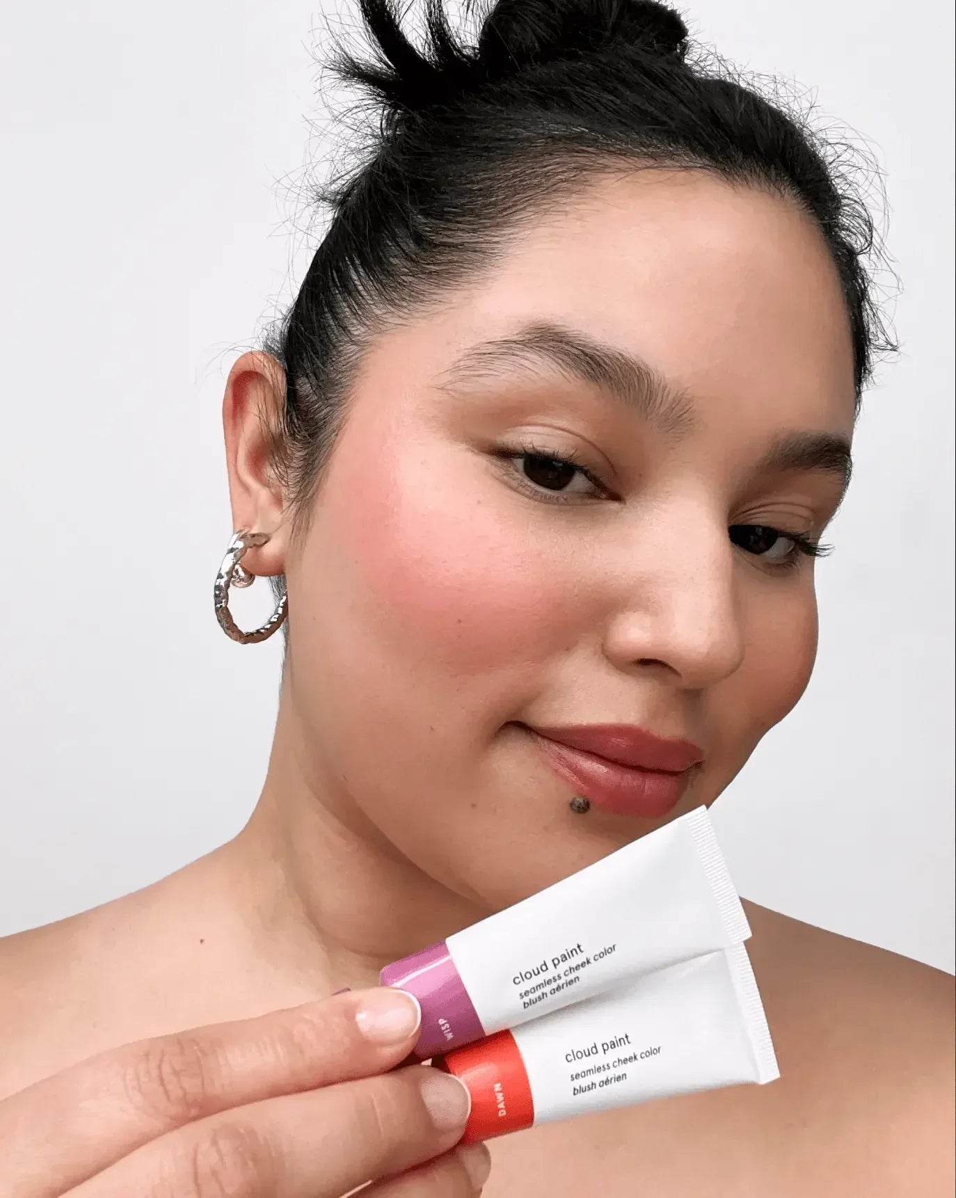 Woman with radiant, dewy pink blush and creamy coral and mauve Cloud Paint blush tubes