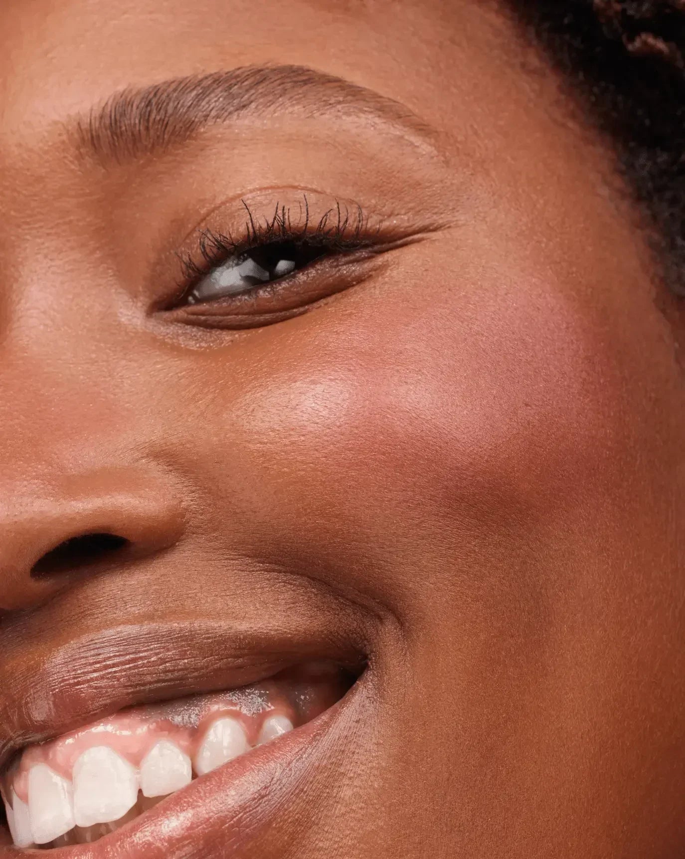Close-up of a smiling face with soft pink blush and dewy finish on the cheeks.