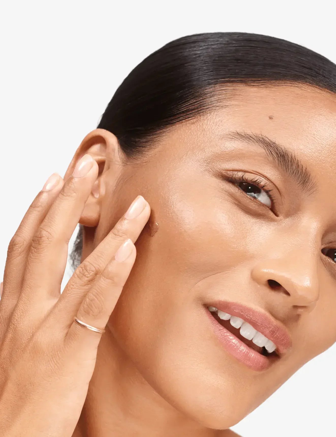 Woman applying peach cream blush with dewy, radiant finish to her cheekbone.