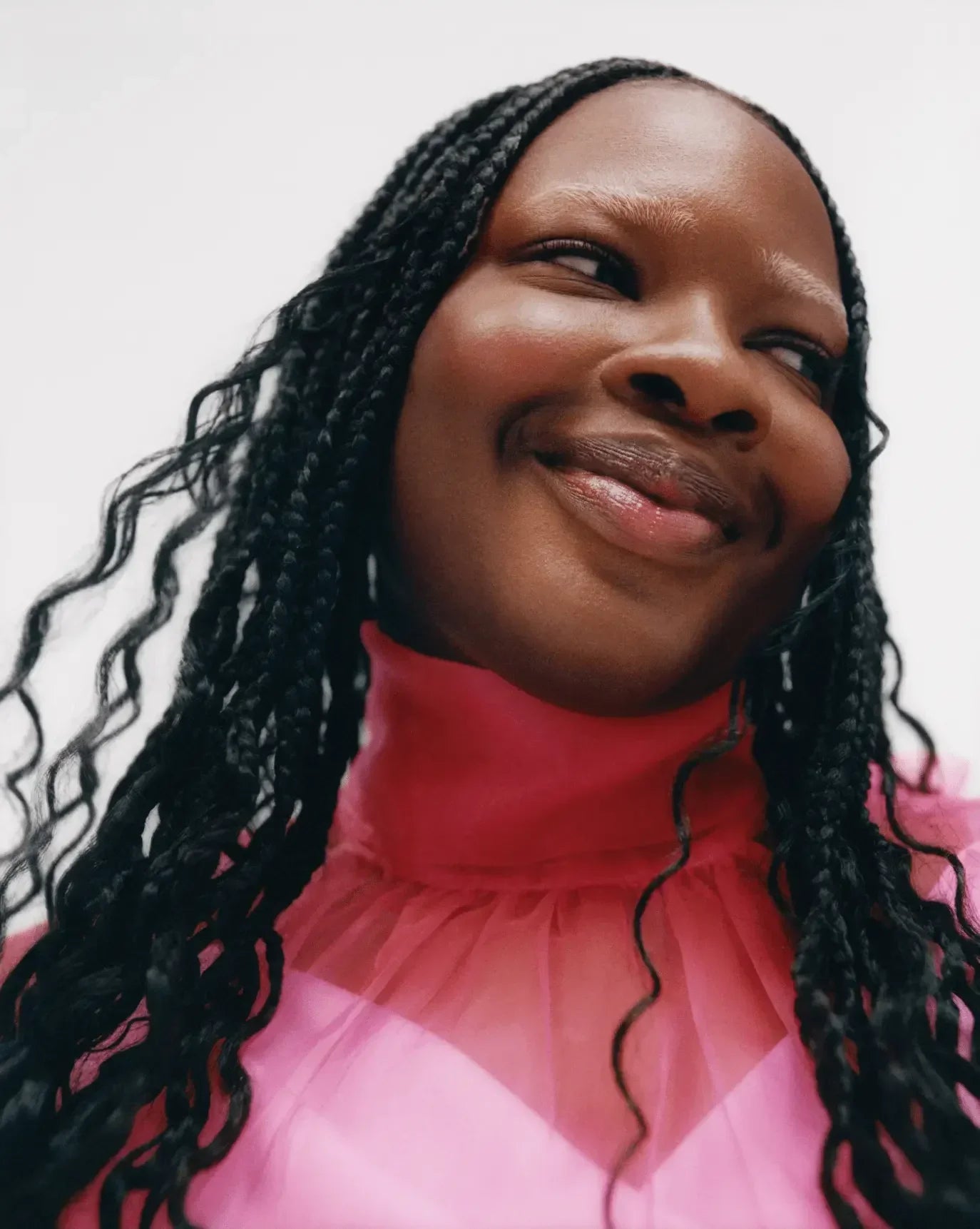 Woman with radiant complexion wearing pink sheer top and subtle dewy blush, braided hair