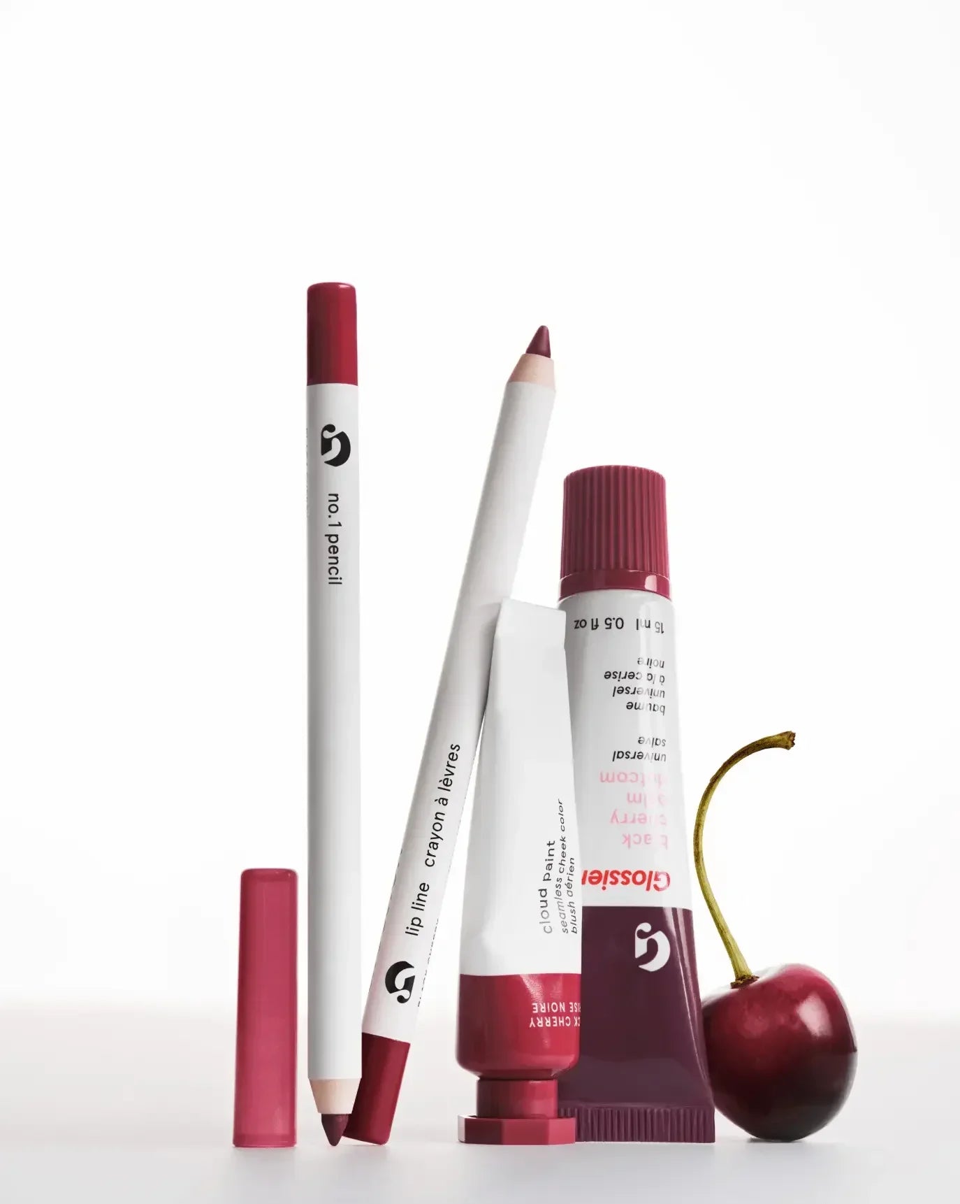 Rich berry makeup set with creamy blush, lip pencils, and a fresh cherry on white backdrop