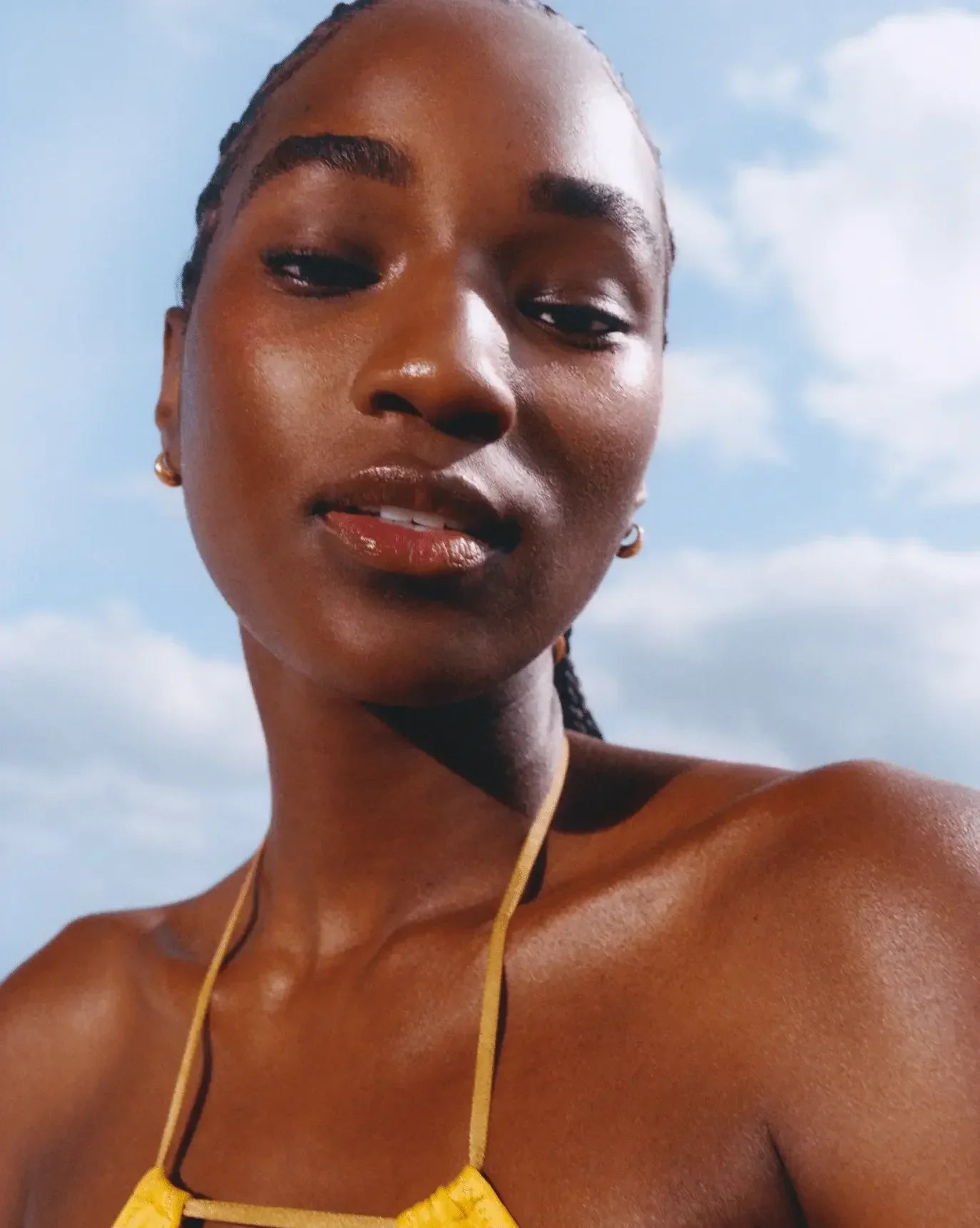 Close-up of a woman with radiant, dewy skin and glossy lips against a blue sky