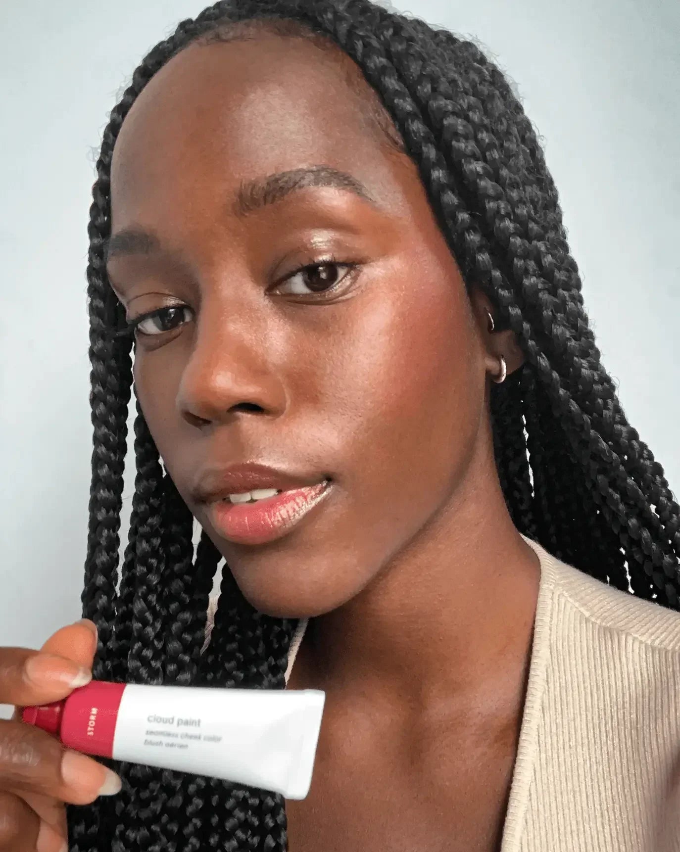 Woman with glowing skin holding tube of blush, showcasing soft rosy cheeks and dewy finish.