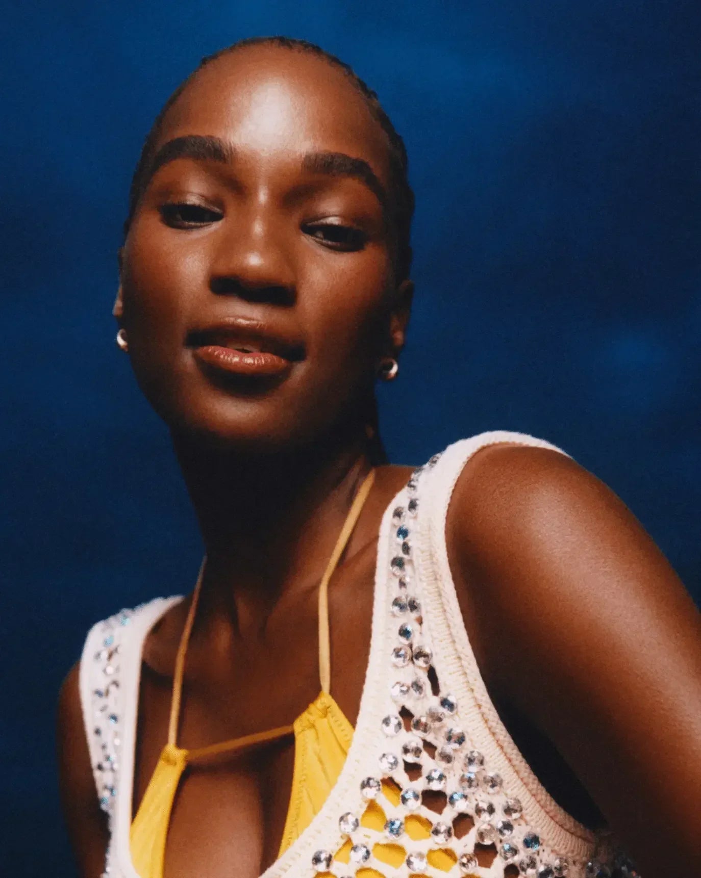 Woman with radiant skin and glossy lips, wearing a jeweled knit top and yellow straps