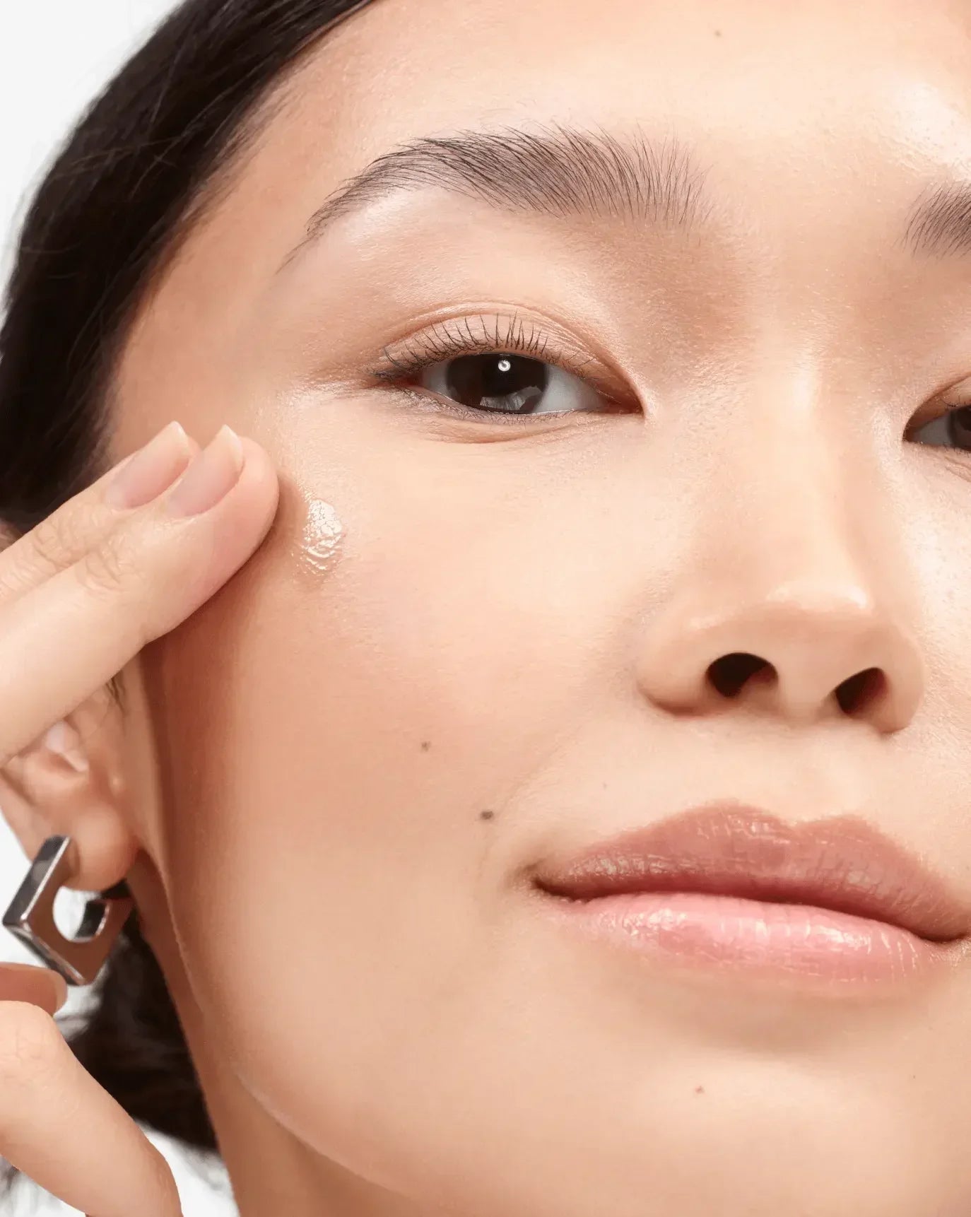 Woman applying creamy, dewy blush to cheek, close-up on radiant skin texture.