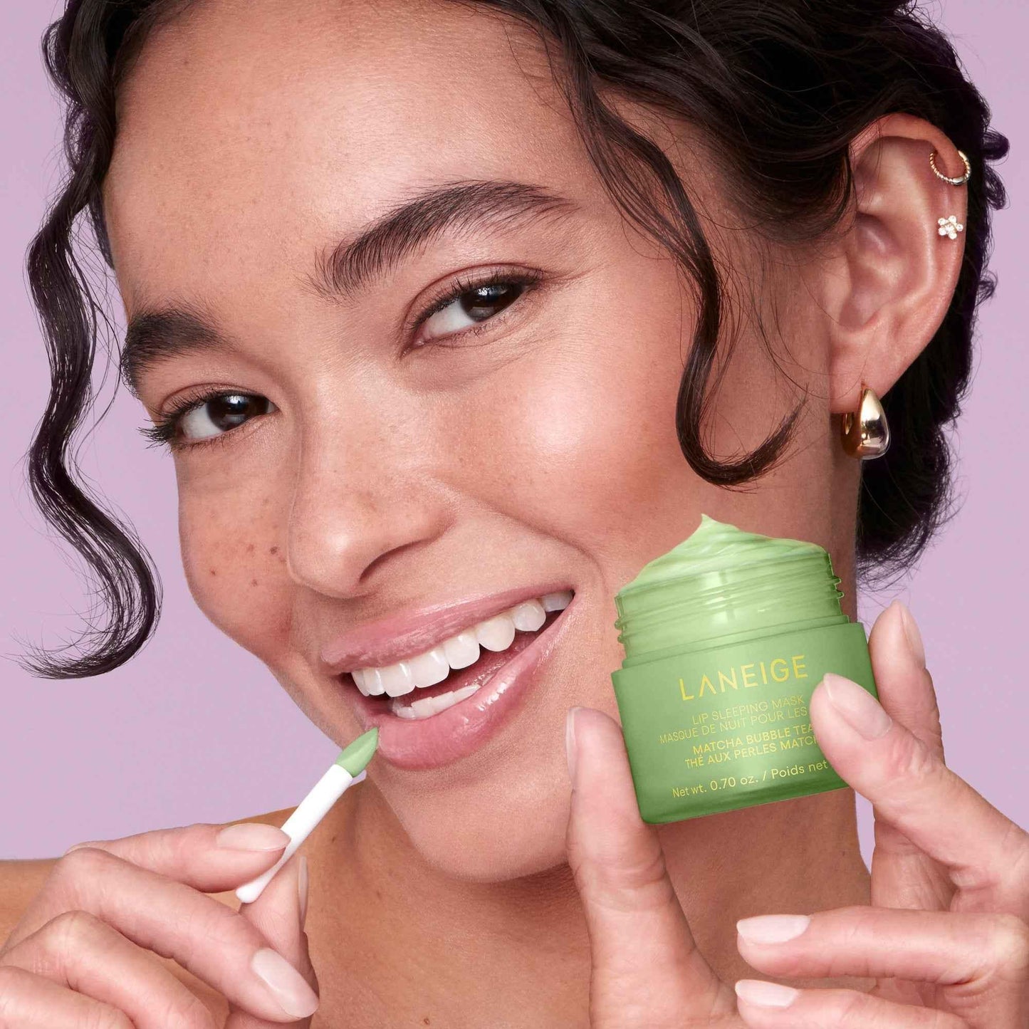 Woman applying green Laneige lip sleeping mask with creamy texture, soft pink background
