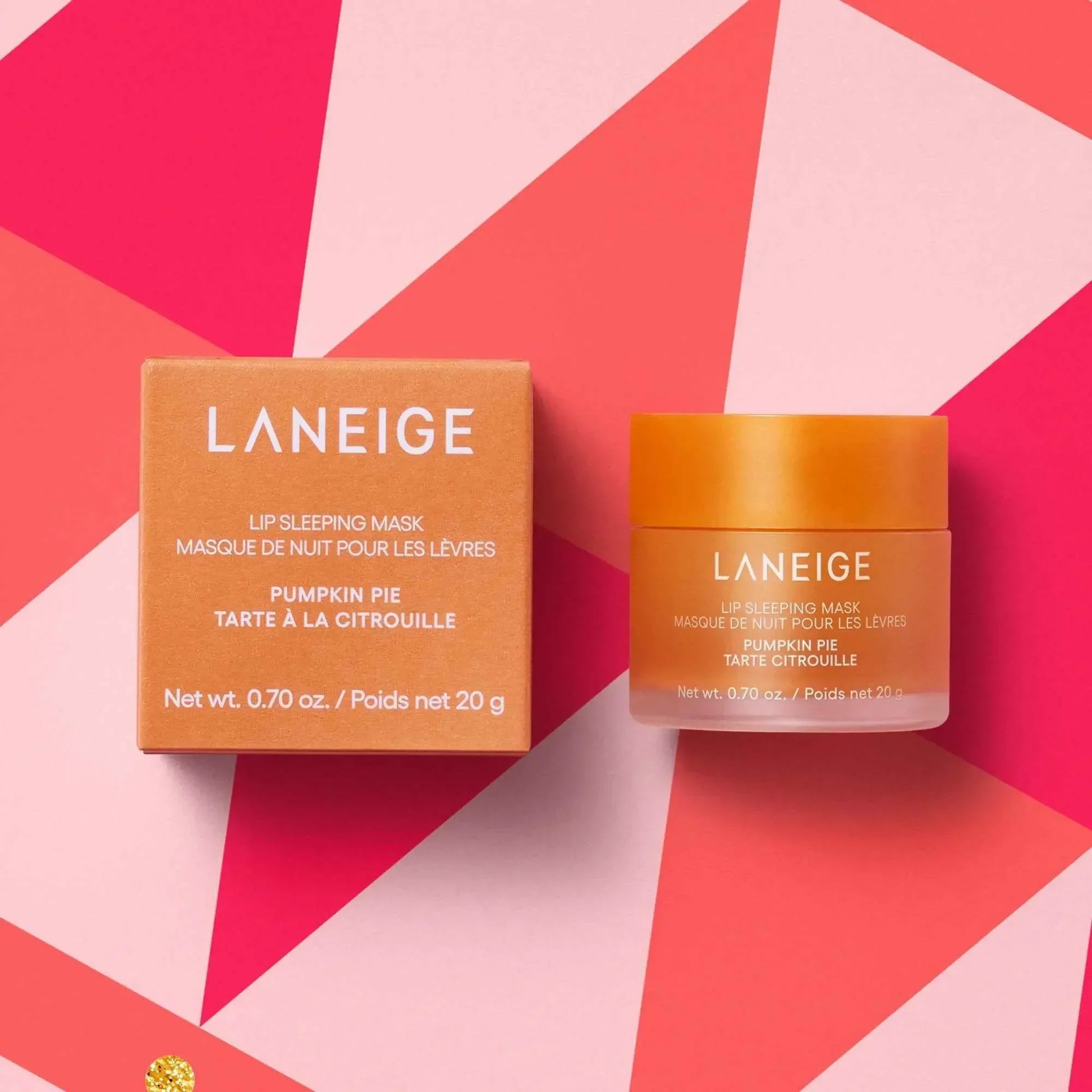 Laneige Pumpkin Pie Lip Sleeping Mask with creamy texture in an orange jar, on geometric pink background.