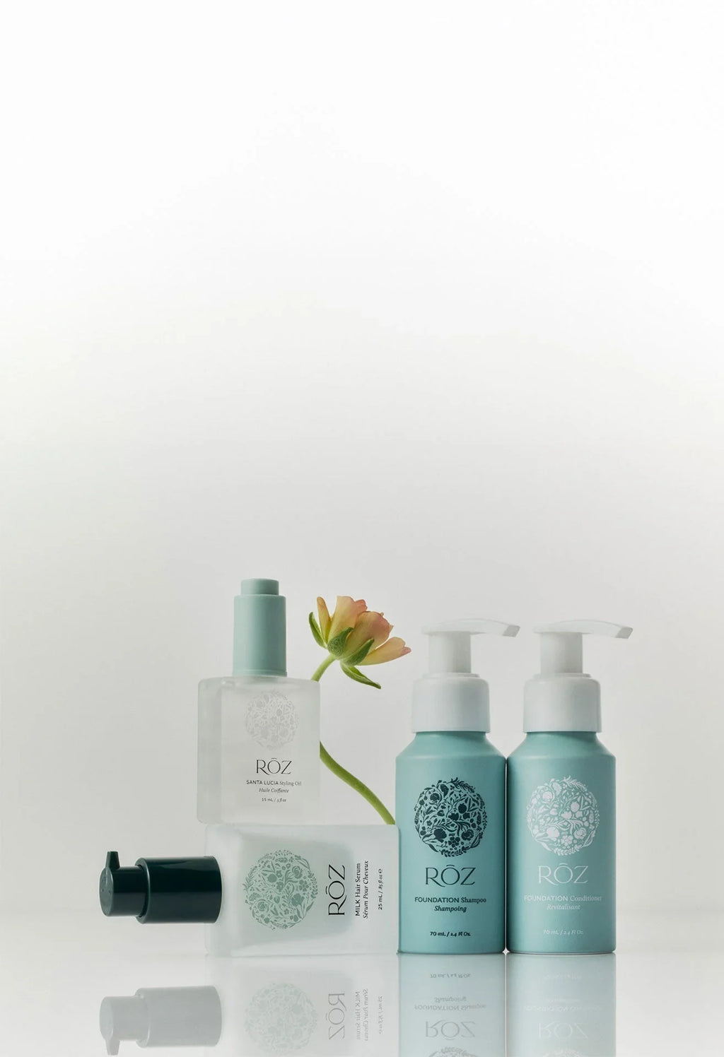 Luxurious ROZ mini essentials kit with pastel blue bottles, dewy glass textures, and soft peach flower on a clean white background, beauty gift set at Wylde Grey.