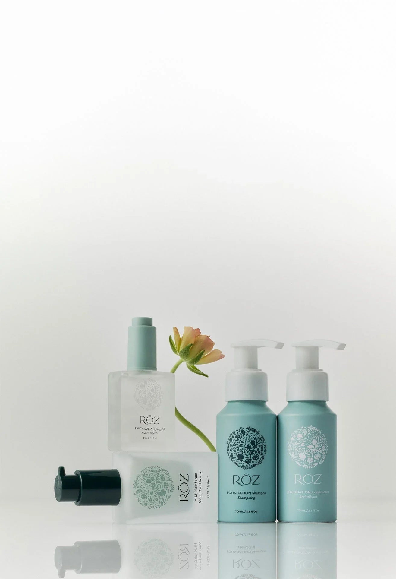 Luxurious ROZ mini essentials kit with pastel blue bottles, dewy glass textures, and soft peach flower on a clean white background, beauty gift set at Wylde Grey.