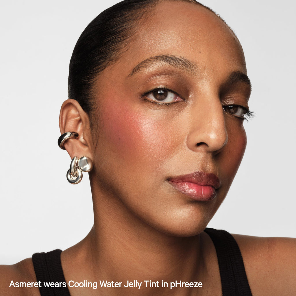 Woman with glowing skin and pink blush, wearing silver earrings, models jelly tint makeup.