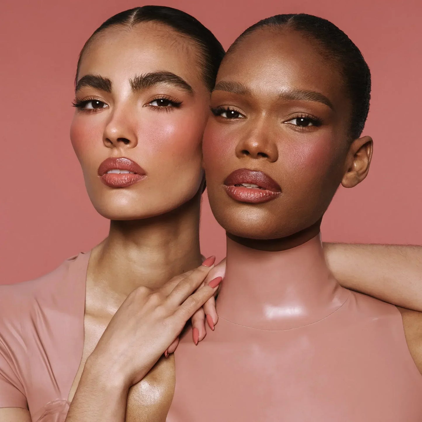 Two women with flawless skin, dewy blush in rose tones, and creamy nude lip color.