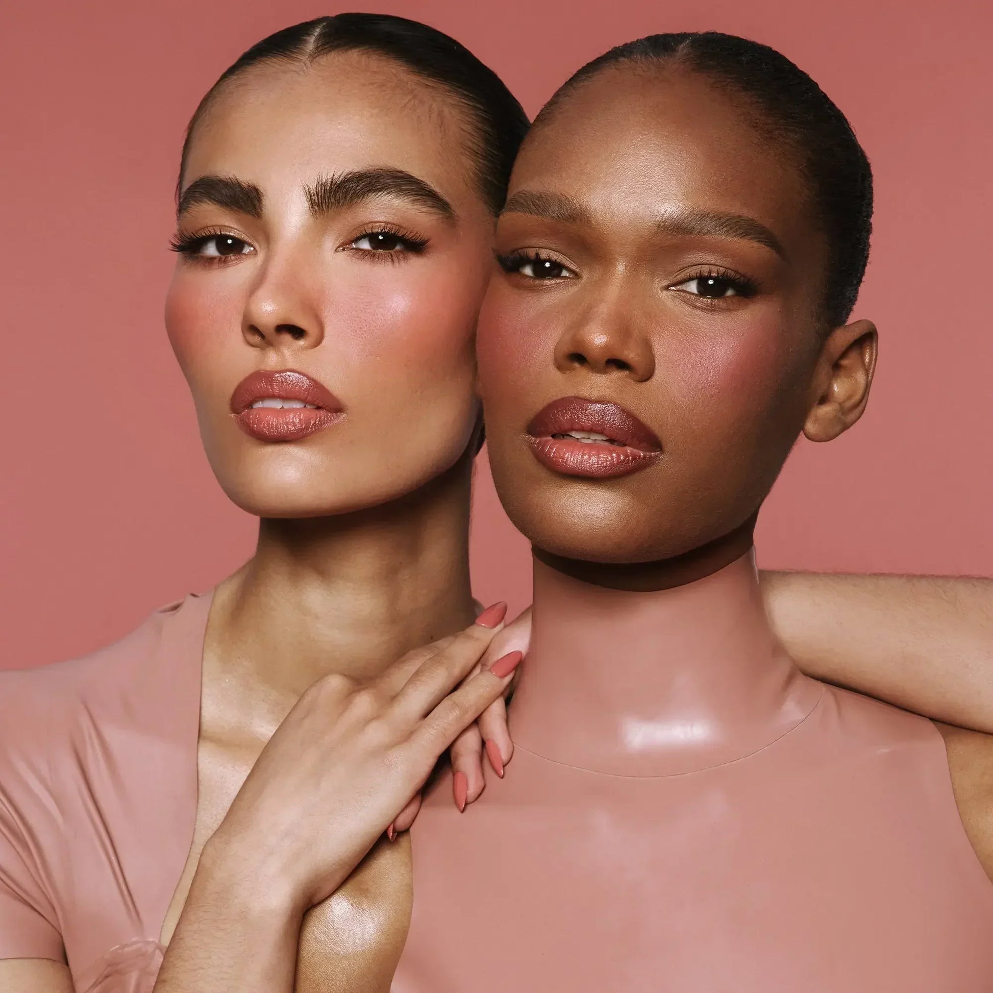 Two women with flawless skin, dewy blush in rose tones, and creamy nude lip color.