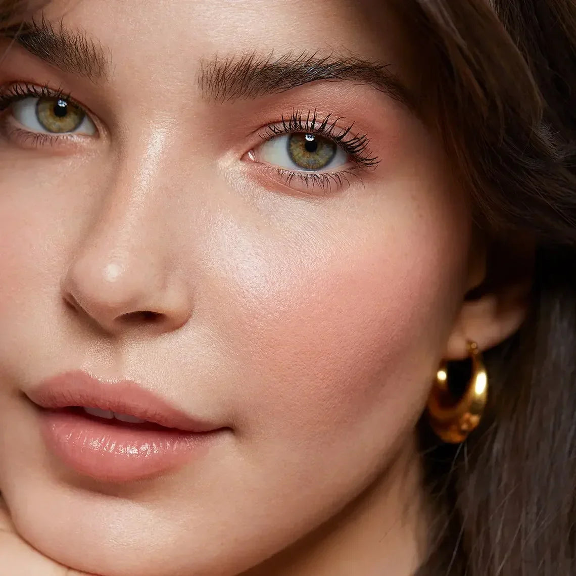 Close-up of a woman with dewy, luminous skin, soft pink blush, and natural nude lips.