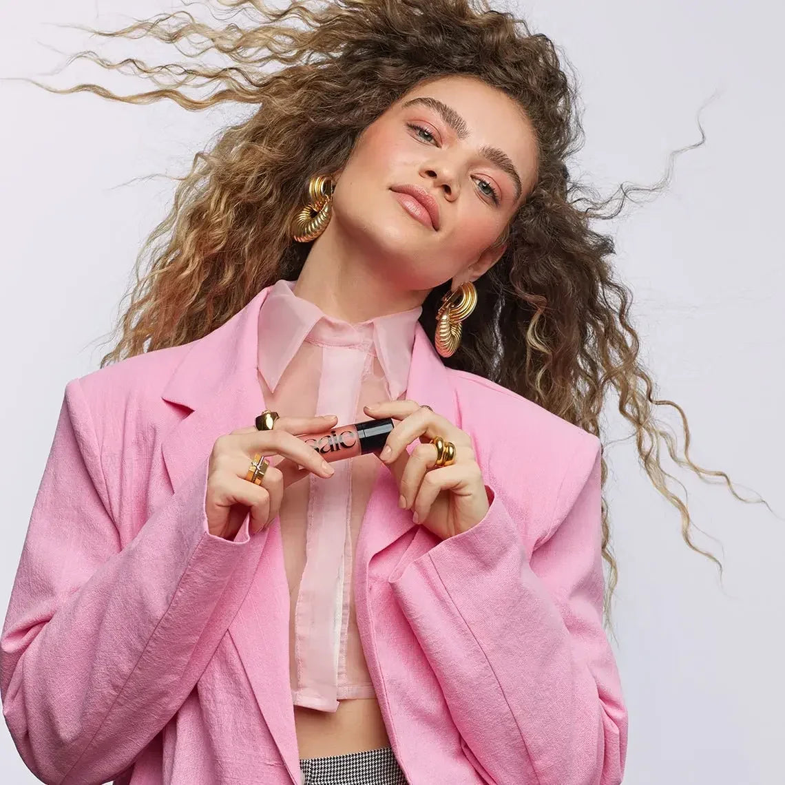 Model with voluminous curls in a pink blazer holding creamy dewy-finish blush tube