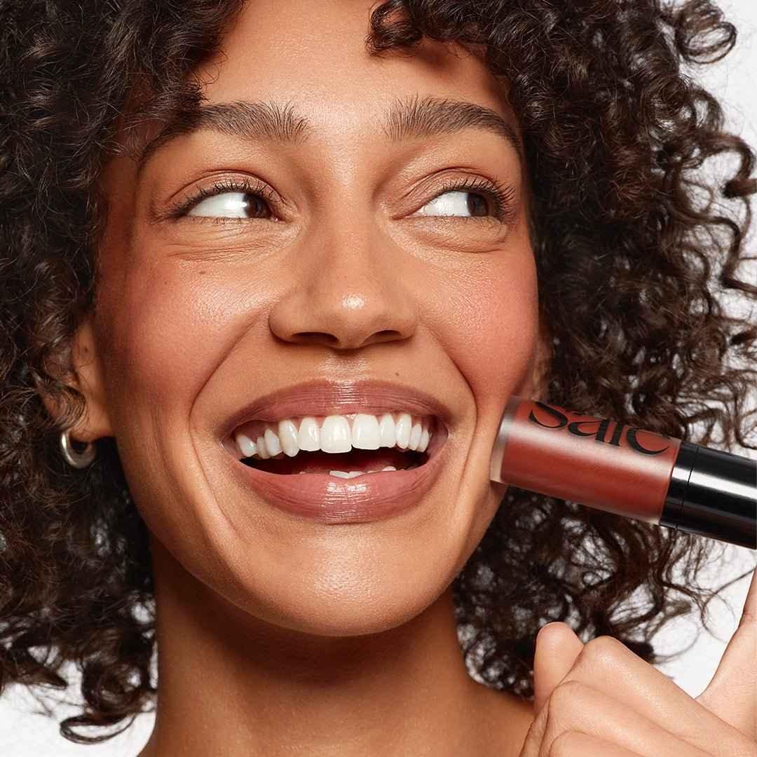 Woman smiling with dewy cheeks, holding rosy cream blush with luxury makeup finish