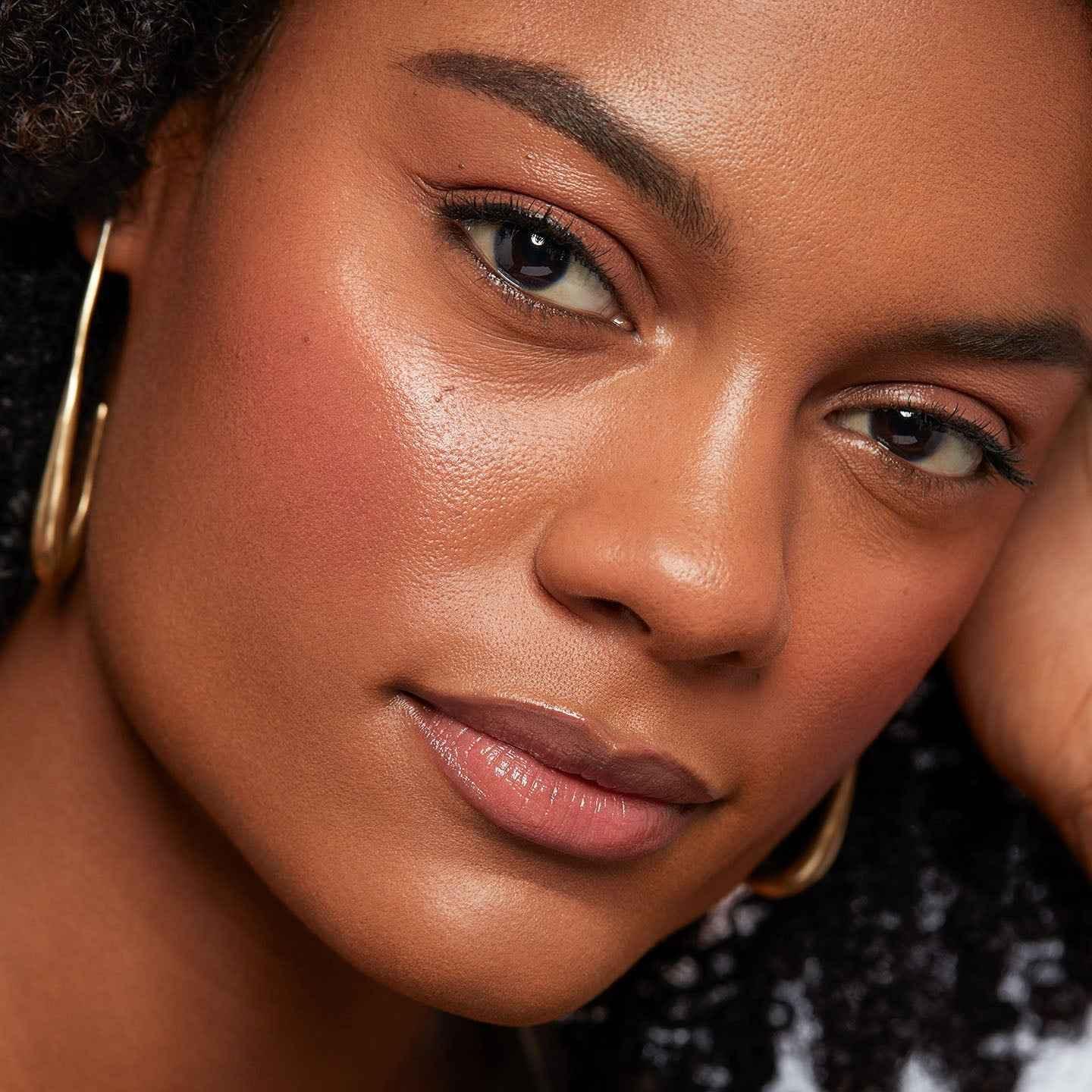 Close-up of woman with glowing skin, dewy blush in rose pink, and soft, natural makeup.
