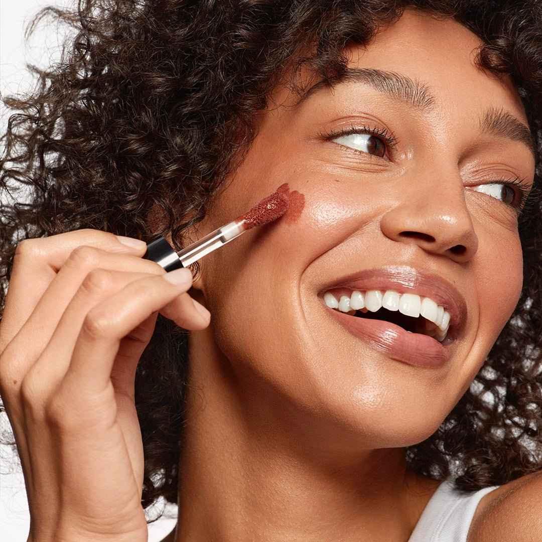 Woman applying creamy blush in a warm rose shade for a radiant, dewy finish on cheeks.