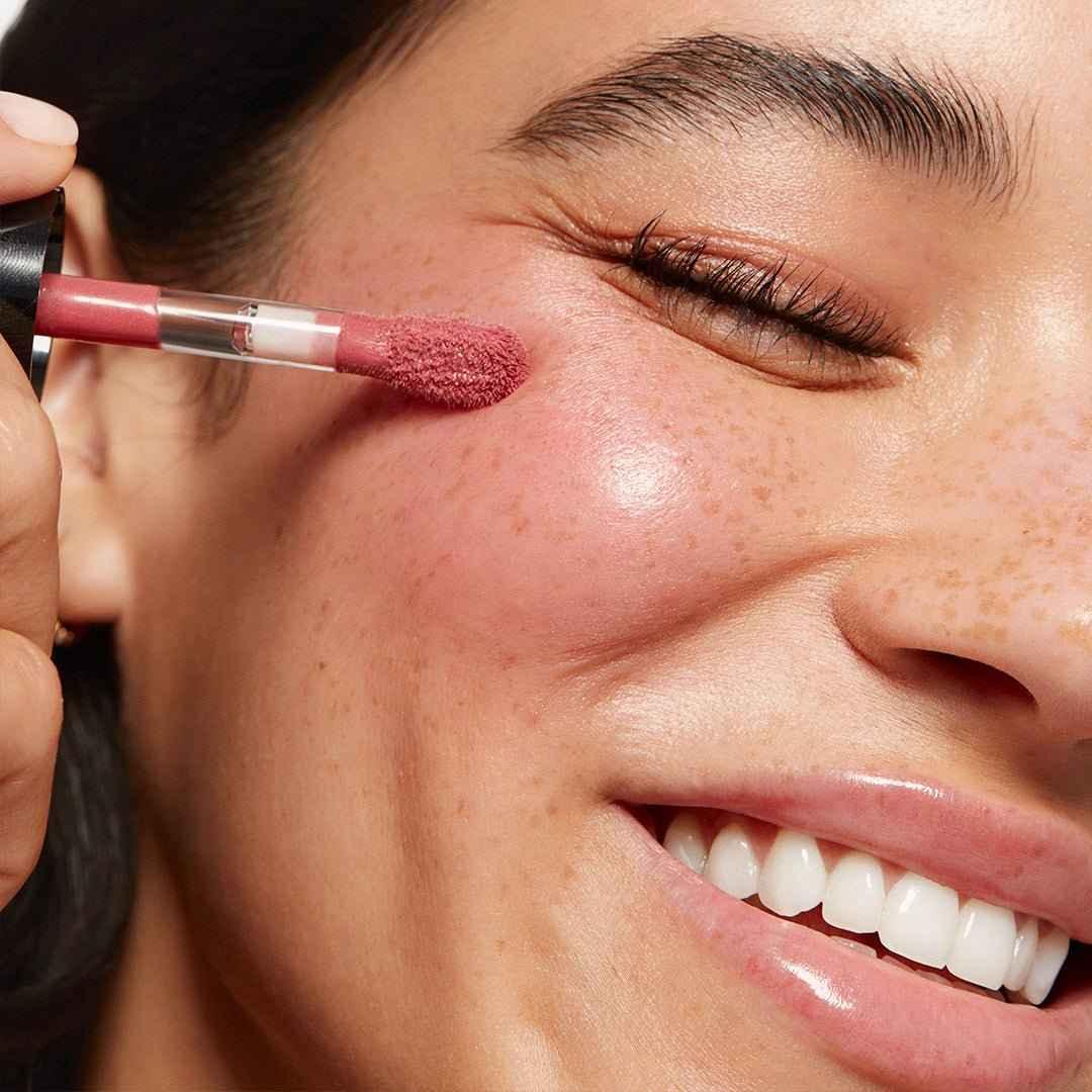 Close-up of dewy rose blush being applied to cheek, highlighting radiant, glowing skin