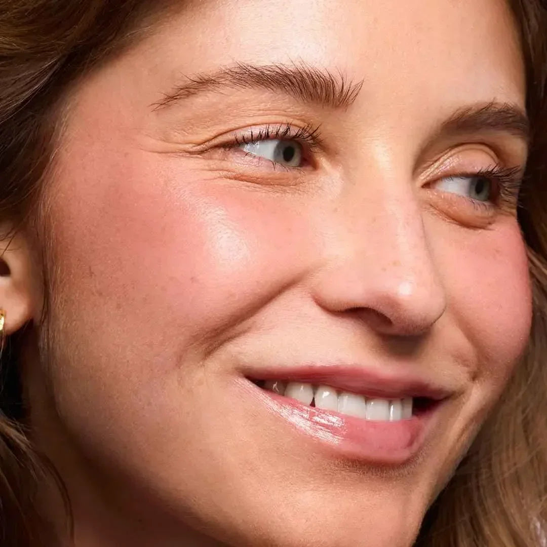 Close-up of a smiling woman with rosy, dewy blush and radiant, natural skin texture.