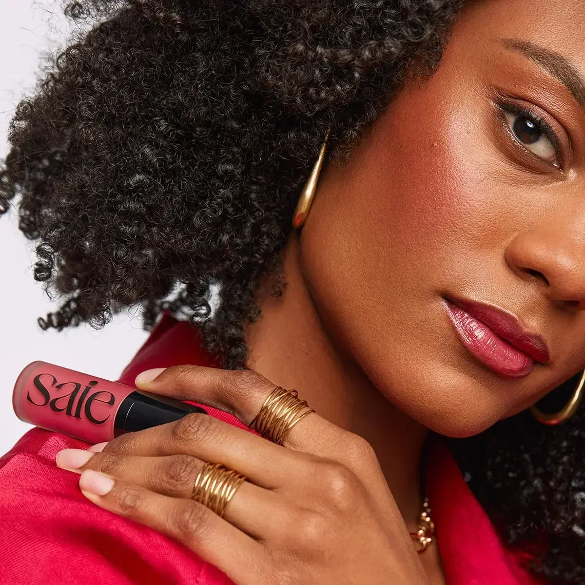 Woman with radiant, dewy blush and rose-toned lips holding pink cream blush tube