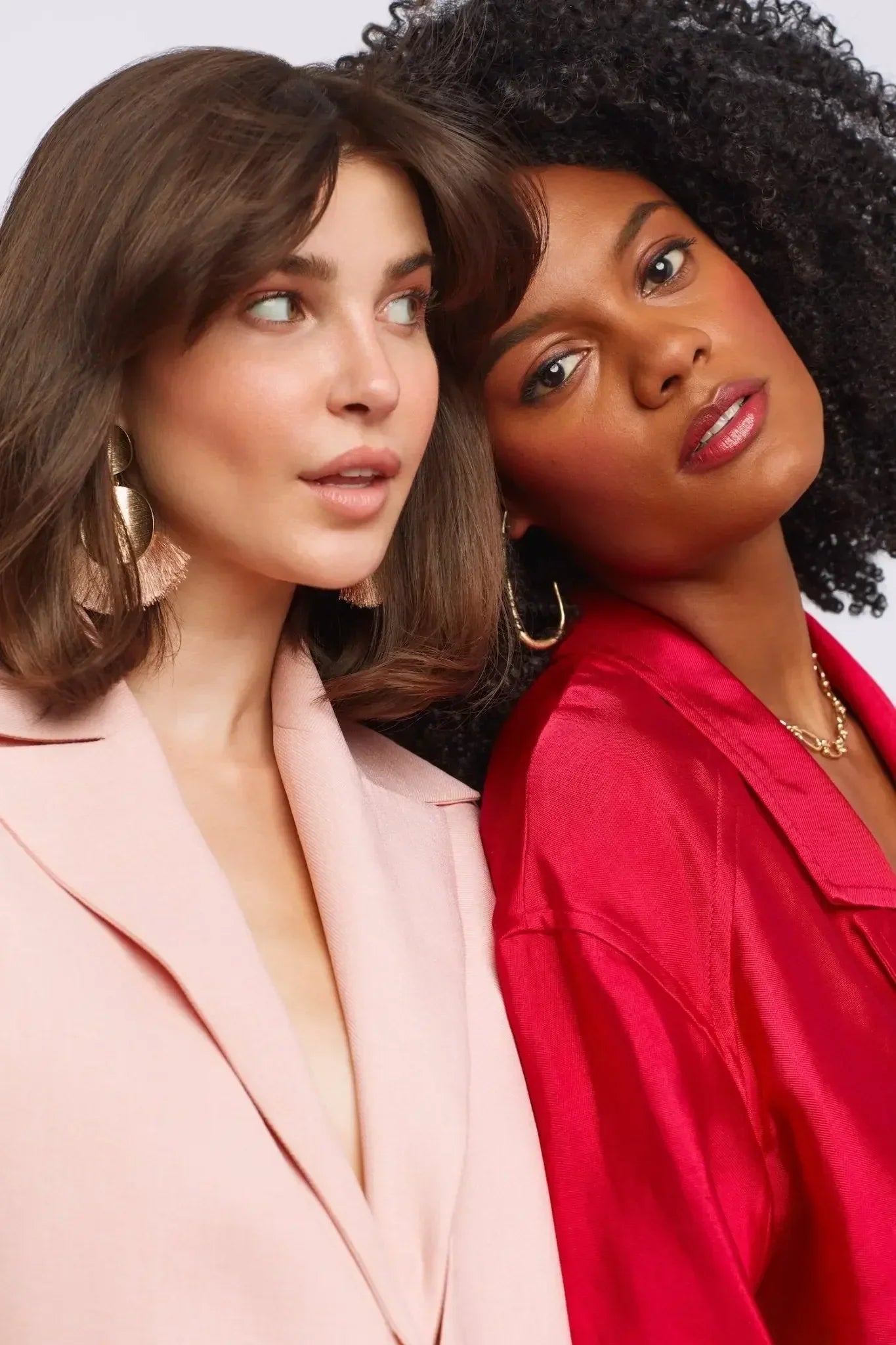 Two women wearing dewy blush makeup, one in a pale pink blazer, the other in red satin, with radiant skin.