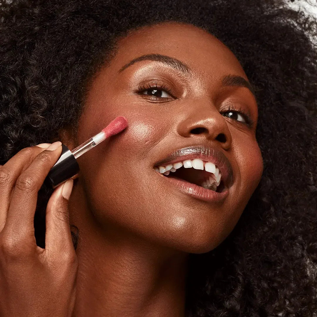 Woman applying rosy pink dewy blush with creamy texture to her cheek