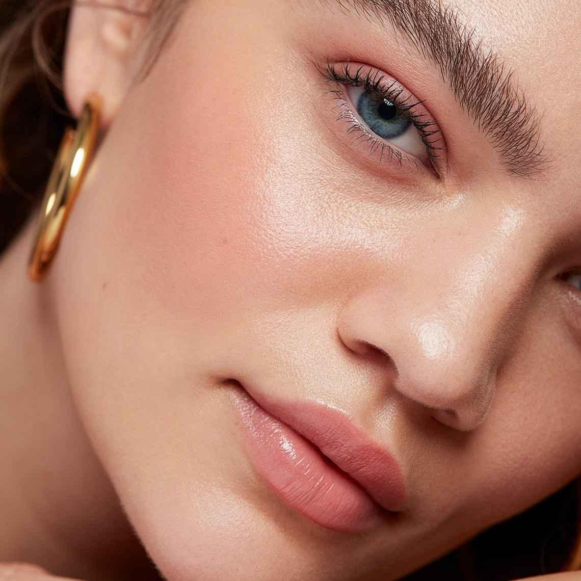 Close-up of dewy makeup look with soft pink blush, creamy texture, and luminous finish on skin.