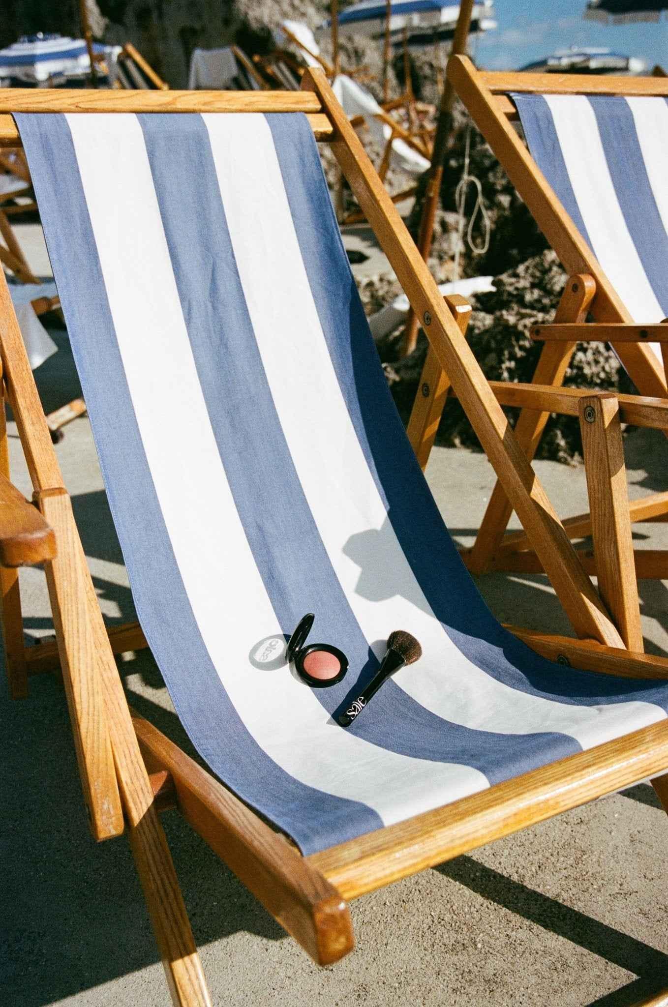 Luxury powder blush in pink shade with soft brush on striped lounge chair outdoors