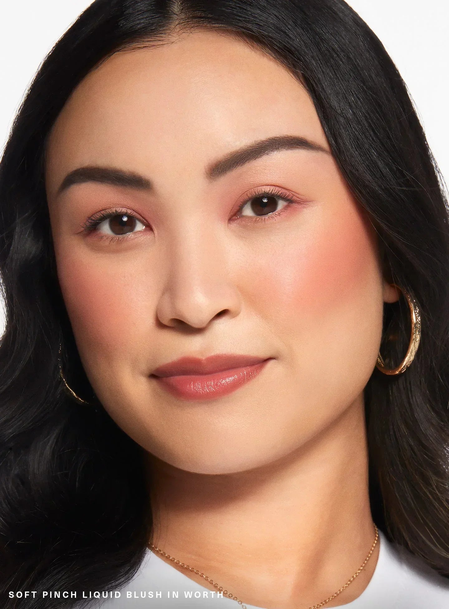 Worth| A model wearing Rare Beauty's Soft Pinch Liquid Blush in the dewy true rose shade "Worth."