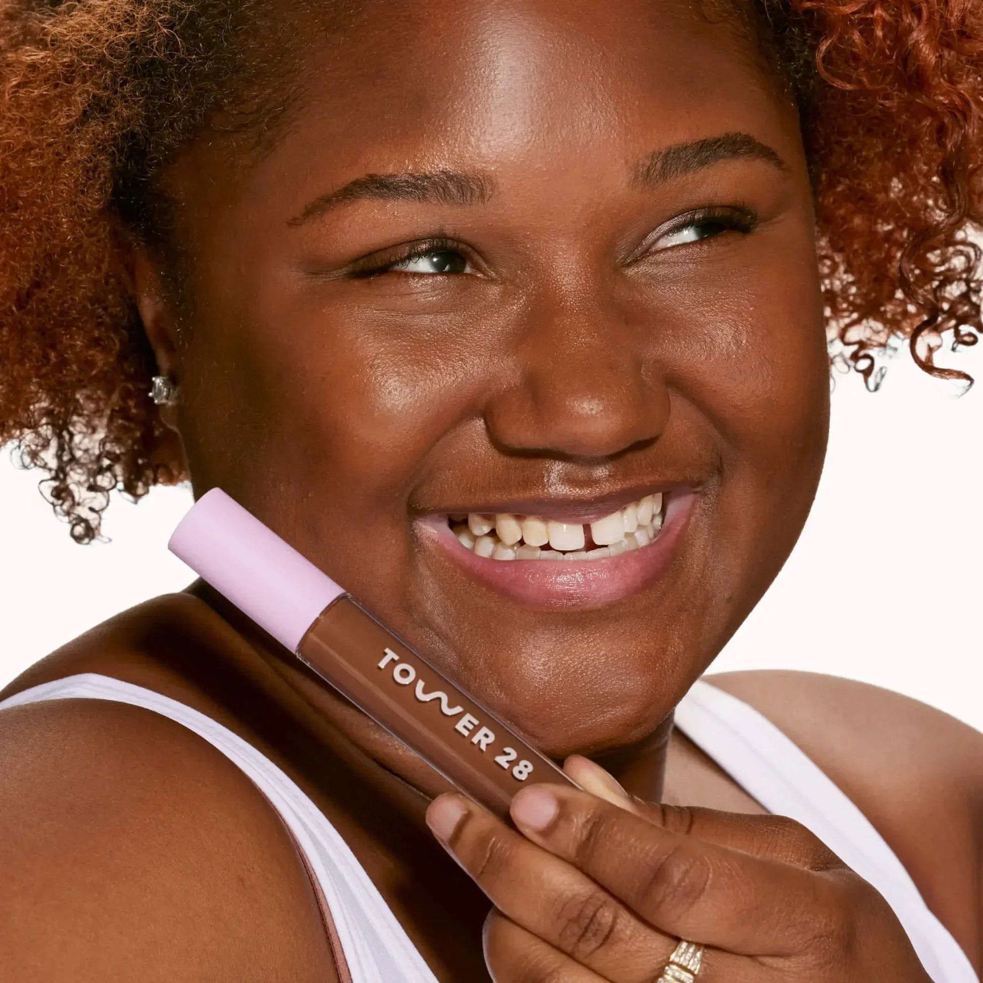 Woman with radiant skin holding creamy dark brown concealer with dewy finish