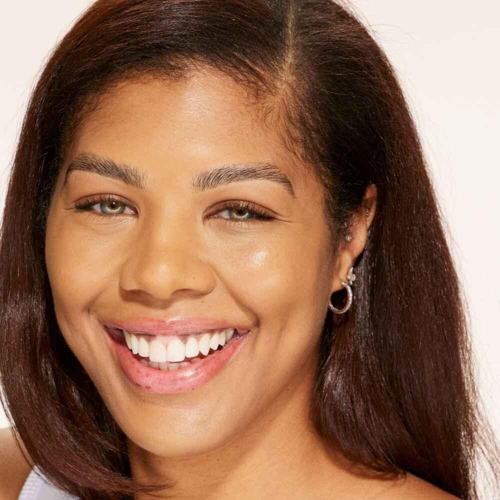 Smiling woman with smooth, radiant skin and a dewy finish, showcasing natural makeup look.