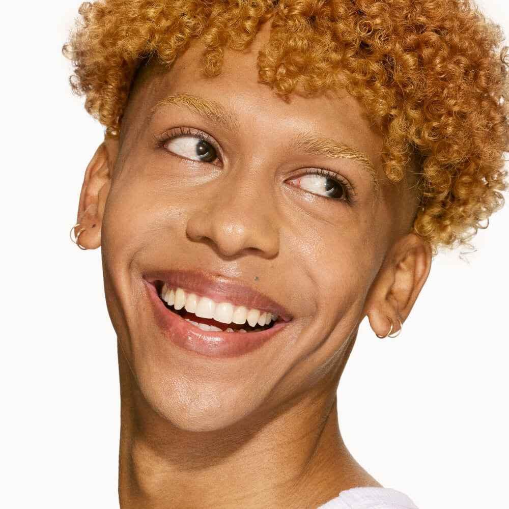 Smiling person with glowing skin and defined brows, showcasing a dewy, flawless complexion.