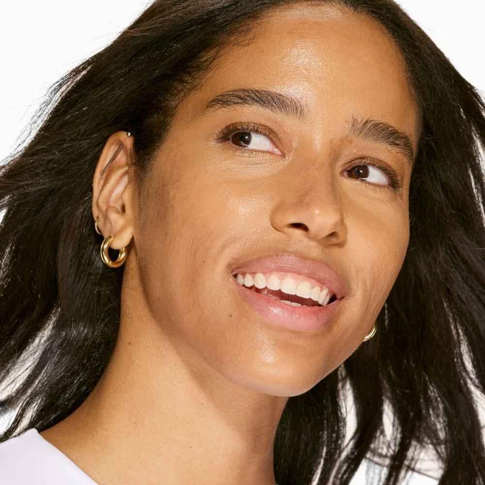 Woman with smooth, radiant skin and dewy finish, wearing natural makeup and gold hoop earrings