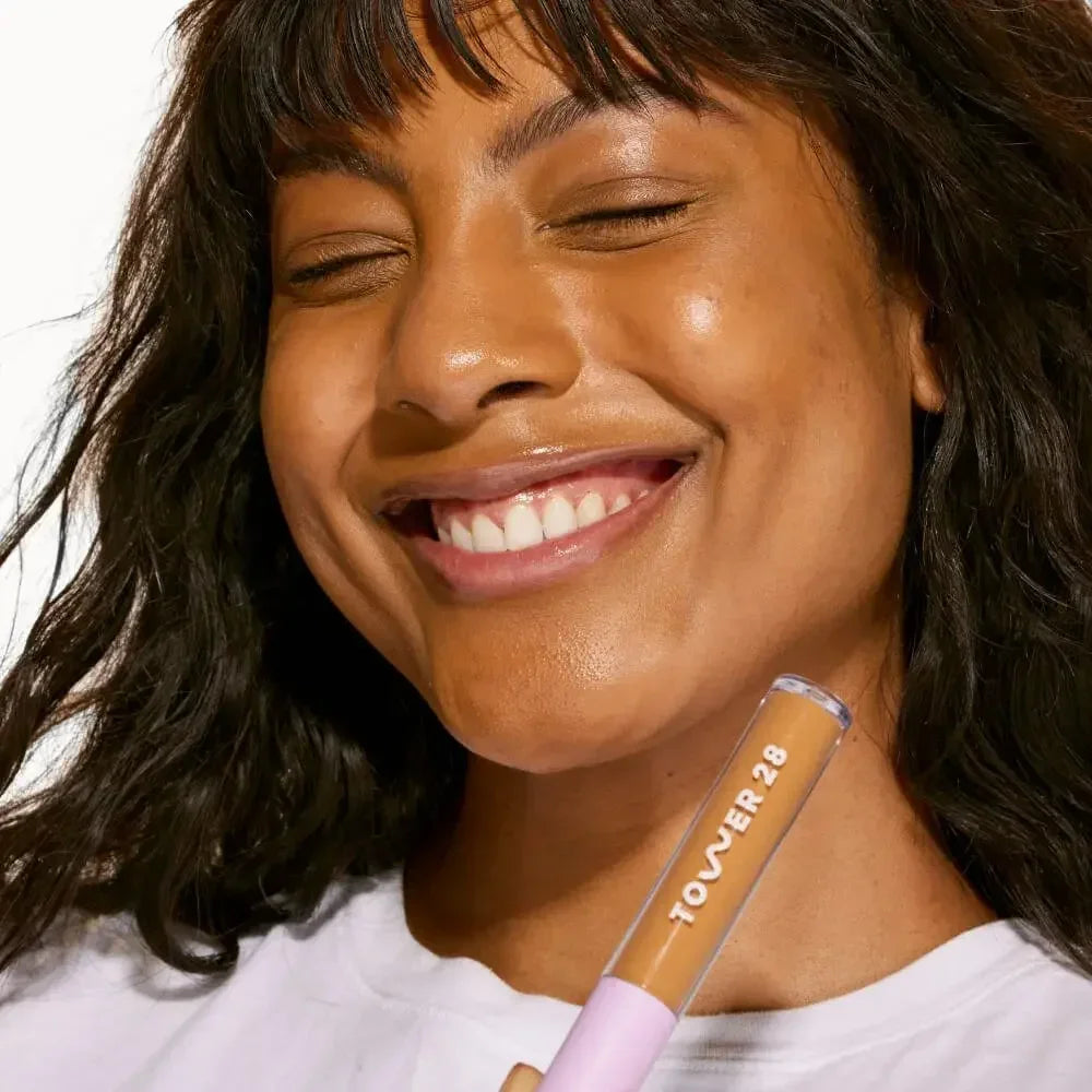 Woman with radiant, dewy skin holding creamy liquid concealer in warm shade