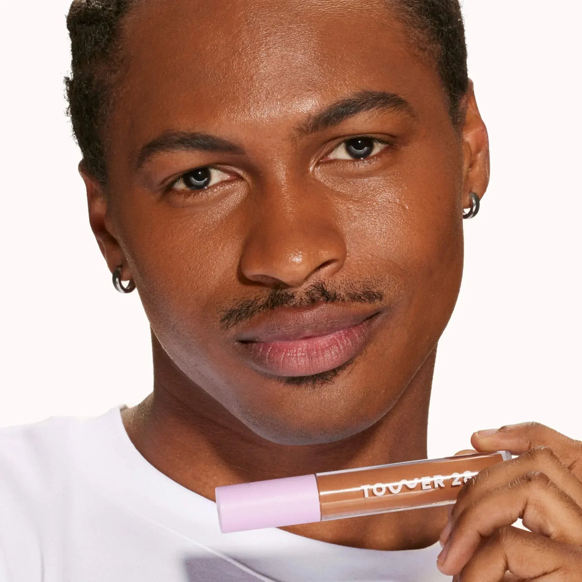 Model holding Tower 28 concealer with creamy texture and dewy finish on smooth skin